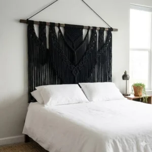 Gothic-inspired black macrame wall art styled above a bed with white linen for high-contrast decor.