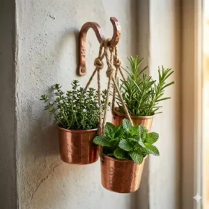 Fresh basil, rosemary, and mint growing in copper planter hangers mounted on a bright kitchen wall near a window.